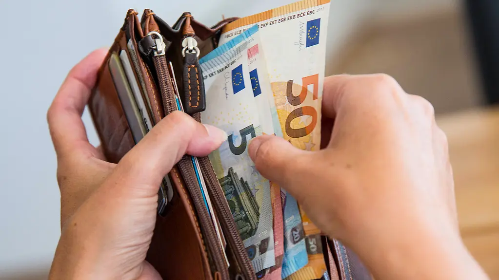 Jemand hält ein Portemonaie mit Geldscheinen in den Händen.