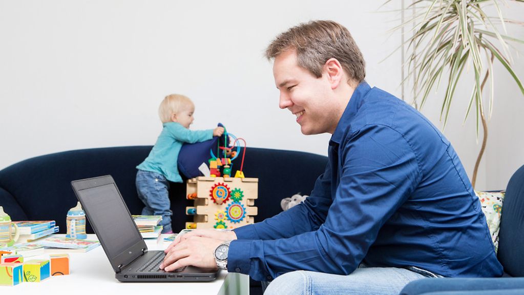 Vater bei der Arbeit an seinem Laptop, im Hintergrund spielen seine zwei Kinder.