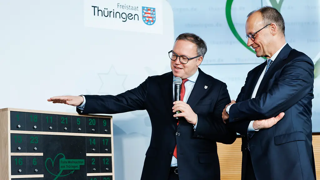 Kanzler Merz wird von Ministerpräsident Voigt ein Adventskalender überreicht.