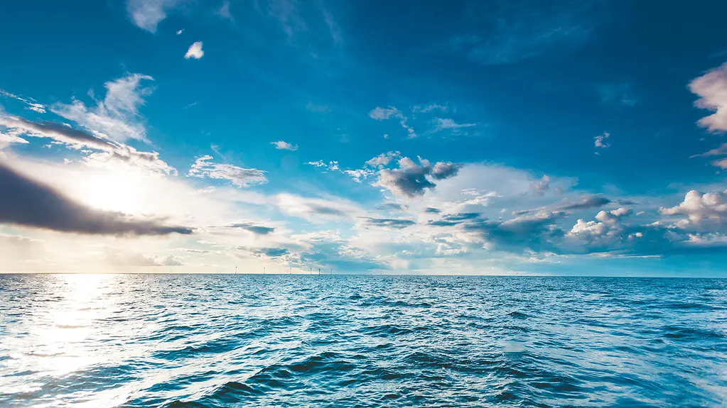 Sonnenstrahlen fallen durch Wolken auf die Wasseroberfläche des Ozeans bei blauem Himmel und blauem Wasser bei seichtem Wellengang.