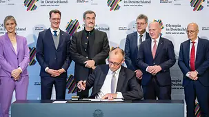 Das Foto zeigt Bundeskanzler Friedrich Merz bei der Unterzeichnung einer Vereinbarung für eine deutsche Bewerbung um Olympische und Paralympische Spiele.