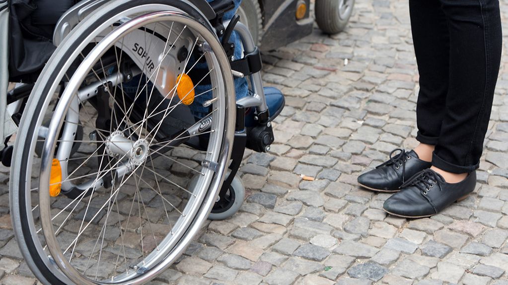 Ein Mann im Rollstuhl neben einer Frau in flachen Schuhen.