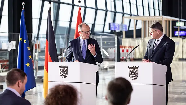 Das Foto zeigt Kanzler Merz und Hessens Ministerpräsident Boris Rhein bei einem Pressestatement am Flughafen Frankfurt.