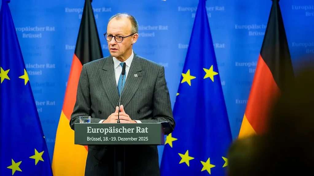 Bundeskanzer Merz am Rednerpult vor europäischen und deutschen Flaggen