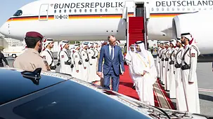 Das Foto zeigt Bundeskanzler Friedrich Merz beim Empfang in Katar auf einem Rollfeld. Im Hintergrund ist der Regierungsflieger zu sehen.