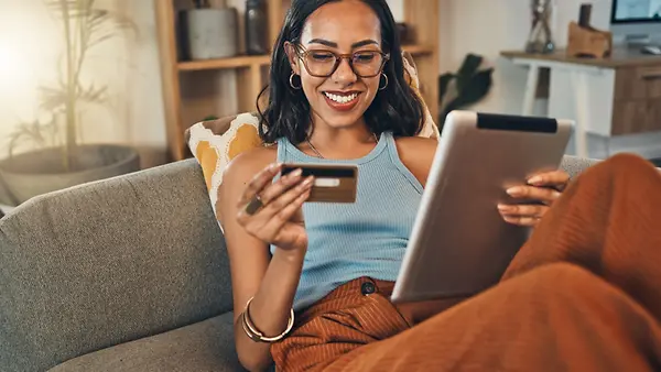 Eine lächelnde Frau nutzt zu Hause ihre Kreditkarte für Online-Einkäufe auf einem Tablet.