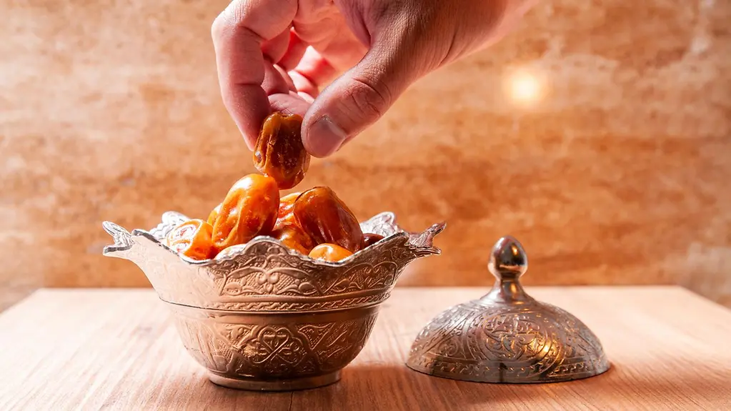 Hand greift in Silberschale mit getrockneten Datteln.
