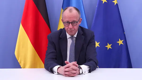 Bundeskanzler Merz sitzt an einem Schreibtisch und schaut in die Kamera. Hinter ihm, von links nach rechts, sind die deutsche, die ukrainische und die europäische Flagge zu sehen.