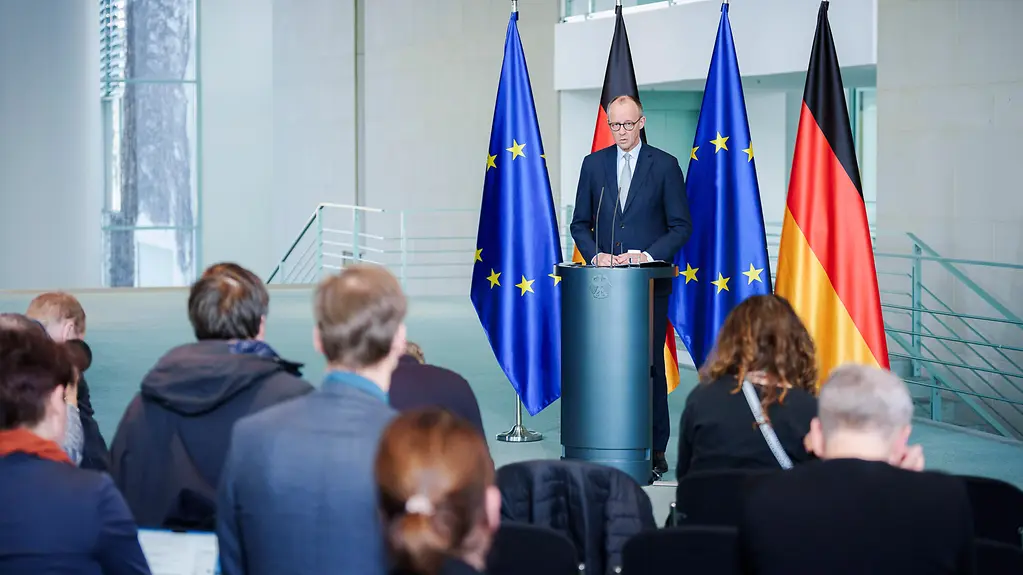 Kanzler Merz vor Pressevertreterinnen und -vertretern am Rednerpult vor Flaggen im Kanzleramt.