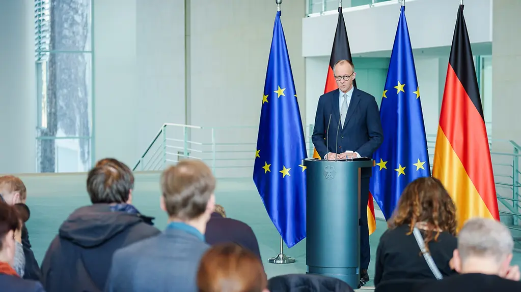 Le chancelier fédéral Friedrich Merz à la tribune devant des représentants de la presse, sur fond de drapeaux à la Chancellerie fédérale.