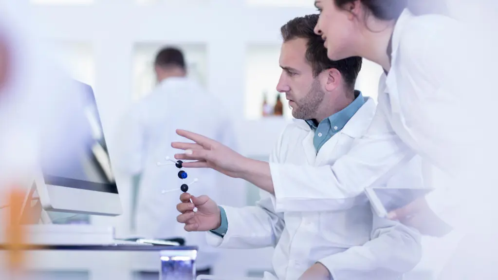 Wissenschaftler mit Molekülmodell am Computer.