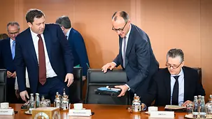 Bundeskanzler Friedrich Merz legt seine Unterlagen an seinem Platz ab vor Beginn der Kabinettssitzung. Links neben ihm steht Lars Klingbeil, rechts neben ihm sitzt Thorsten Frei.