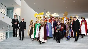 Bundeskanzlerin Angela Merkel geht mit Sternsinger auf einer Treppe.