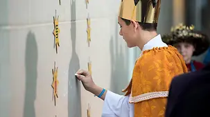 Ein Sternsinger schreibt den Segenspruch mit Kreide an die Wand.
