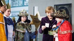 Bundeskanzlerin Angela Merkel gibt den Sternsingern eine Spende.