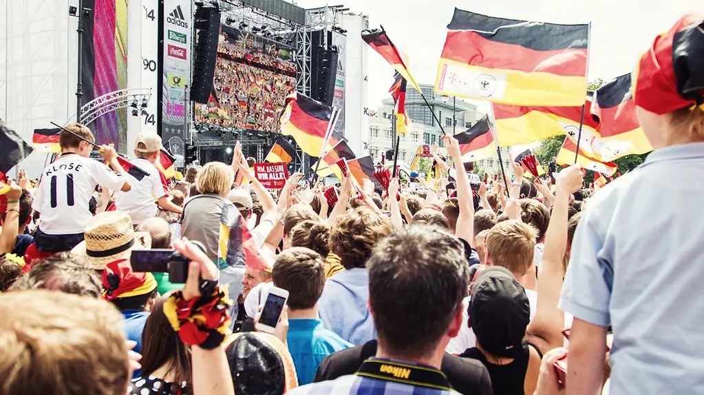 Eine großer Leinwand, vor der Fans mit Deutschland-Flaggen feiern.