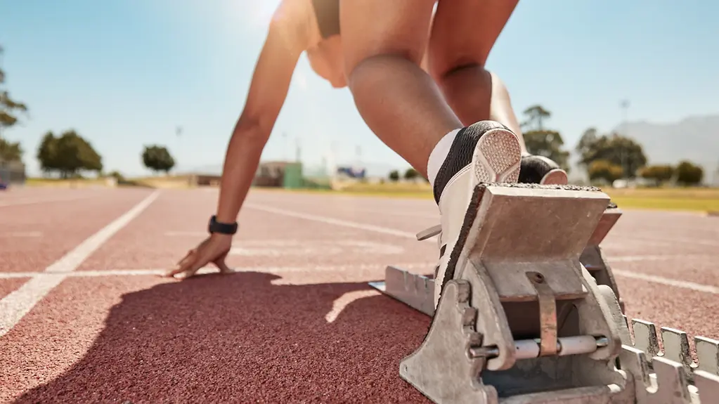 Eine Sportlerin auf einer Laufbahn positioniert sich im Startblock.