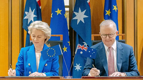 EU-Kommissionspräsidentin Ursula von der Leyen und der australische Premierminister Anthony Albanese sitzen am Tisch und unterzeichnen. Im Hintergrund die australische und die EU-Flagge.
