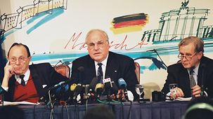 Face à la presse : le chancelier fédéral Helmut Kohl (au centre) entouré du ministre fédéral des Affaires étrangères Hans-Dietrich Genscher (à g.) et du porte-parole du gouvernement fédéral Dieter Vogel ( à dr.)