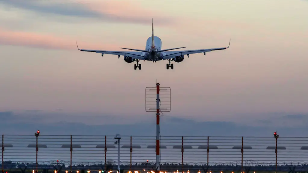 Abflug eines Flugzeugs von einem Flughafen vor einem Abendhimmel.
