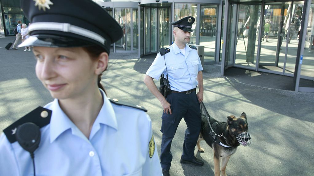 Polizistin und Polizist mit Hund vor einem Gebäude.