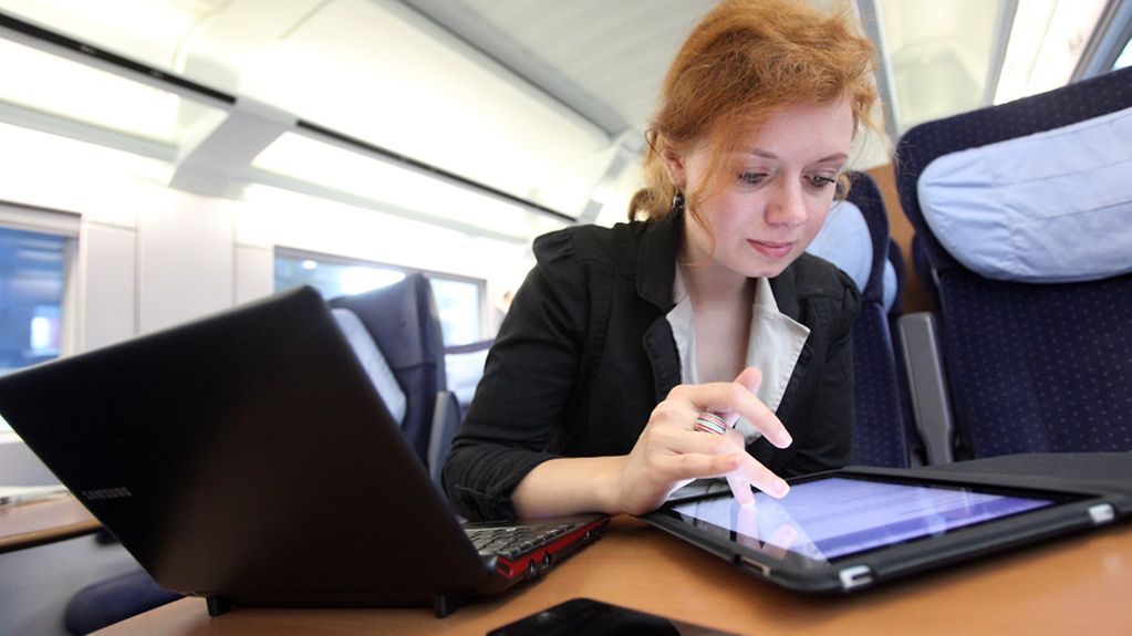 Eine junge Frau in einem Intercity Express (ICE) an einem Tisch und arbeitet mit ihrem iPad