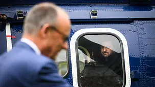 Präsident Selenskyj schaut aus dem Fenster eines stehenden Helikopters. Im Vordergrund Kanzler Merz im Seitenprofil.