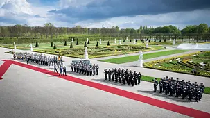 The Federal Chancellor and the Brazilian President inspect the guard of honour of the Bundeswehr on a red carpet. In the background, the palace gardens of Herrenhausen Palace.