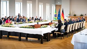 The governments of Germany and Brazil are seated around a large table. Photographers and interpreters in the background.