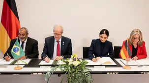 La ministre Alabali Radovan signe un partenariat. À côté d’elle sont assis le ministre brésilien de l’Environnement et deux autres personnes, qui signent également des documents.