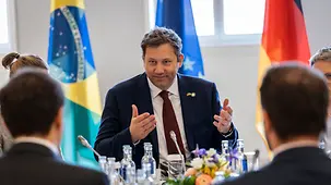 Lars Klingbeil discute autour d’une table. En arrière-plan, les drapeaux du Brésil, de l’Allemagne et de l’UE.