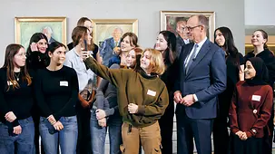 Bundeskanzler in einer Gruppe von Schülerinnen im Bundeskanzleramt. Eine Schülerin nimmt mit ihrem Handy ein Selfie der Gruppe auf.