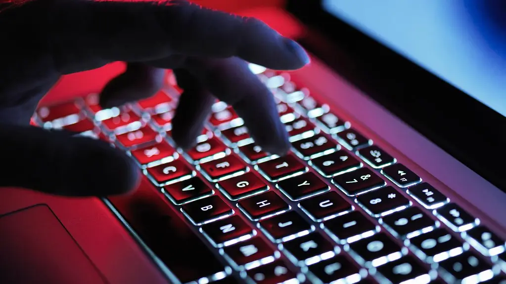 Eine Hand tippt im Dunklen auf einer beleuchteten Tastatur eines Laptops.