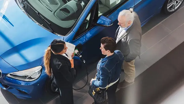 Vogelperspektive auf eine Verkäuferin im Gespräch mit Kunden in einem Autohaus.