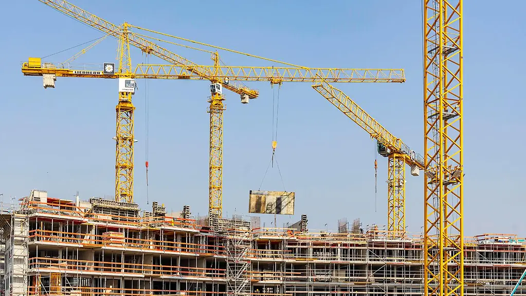 Ein Haus wird gebaut, Kräne sind zu sehen. 