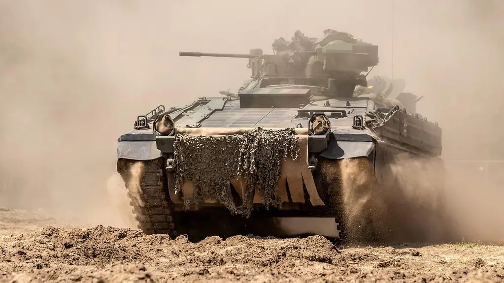 Ein Panzer fährt über eine staubige Straße.