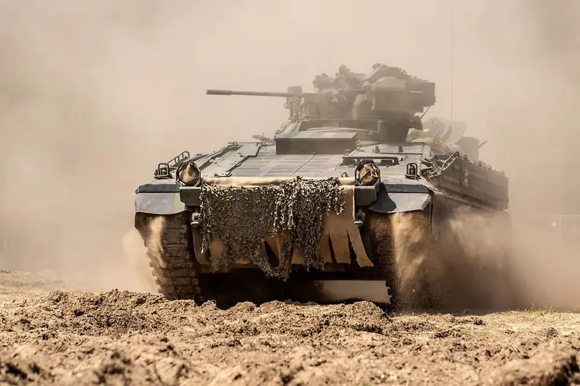 Ein Panzer fährt über eine staubige Straße.