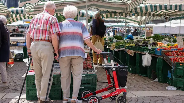 Zwei Senioren stehen mit Gehhilfen und Rollator auf dem Wochenmarkt