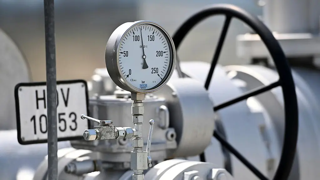 The image shows a gas cylinder and a pressure gauge. The needle indicates a medium level.