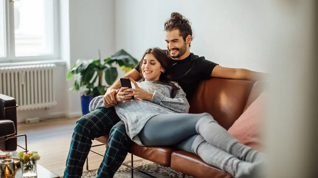 Ein Pärchen sitzen mit einem Smartphone auf dem Sofa.
