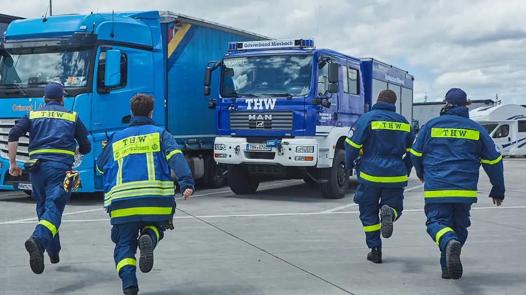 Einsatztruppe des Technischen Hilfswerks Miesbach mit Rettungsfahrzeug in Bereitschaft auf Parkplatz.