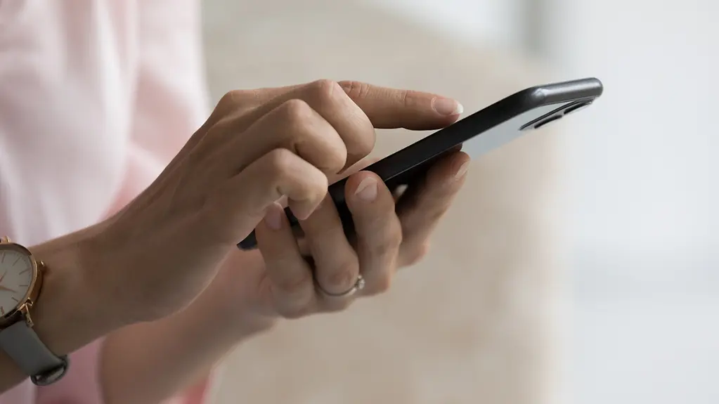 Eine Hand einer Frau hält ein Smartphone. Mit der anderen Hand tippt sie etwas auf dem Display.