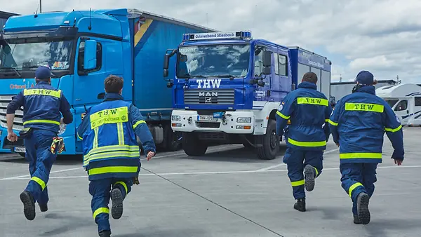 Einsatztruppe des Technischen Hilfswerks Miesbach mit Rettungsfahrzeug in Bereitschaft auf Parkplatz.