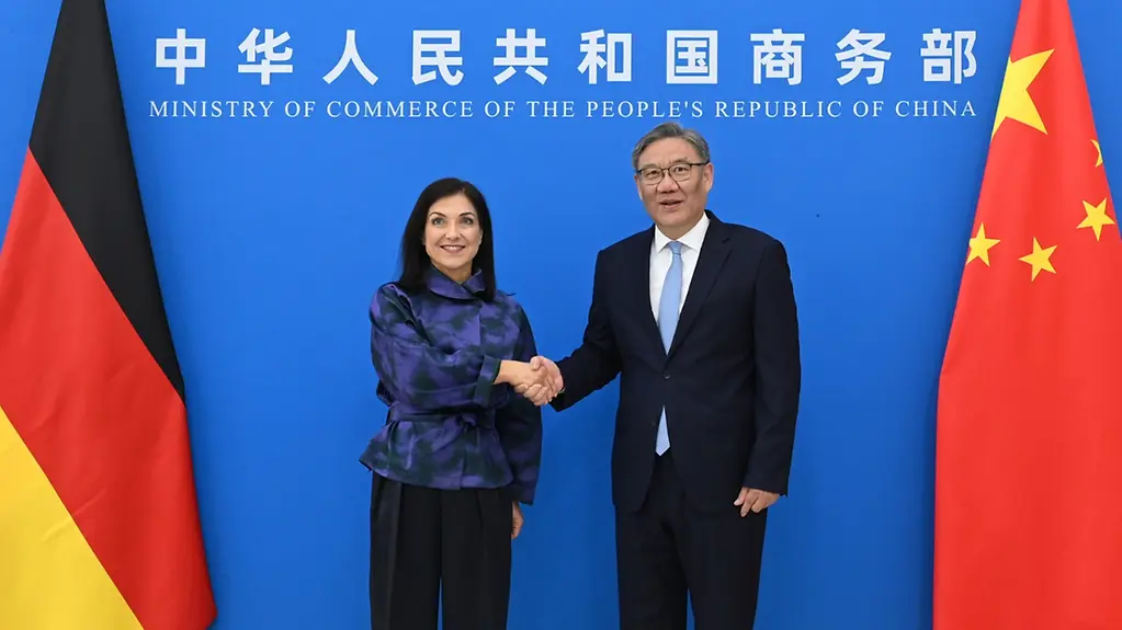 Vor blauer Wand mit Flaggen schütteln Bundeswirtschaftsministerin Katherina Reiche und der chinesische Handelsminister Wang Wentao die Hände. 