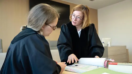 Zwei Richterinnen in Robe schauen in einem Gerichtssaal auf Akten.