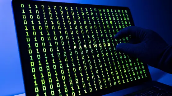 Eine Hand vor einem dunklen Computerbildschirm mit einem binären Zahlencode in grüner Schrift.