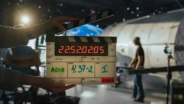 Zwei Hände halten eine geöffnete Filmklappe am Set eines Drehs.