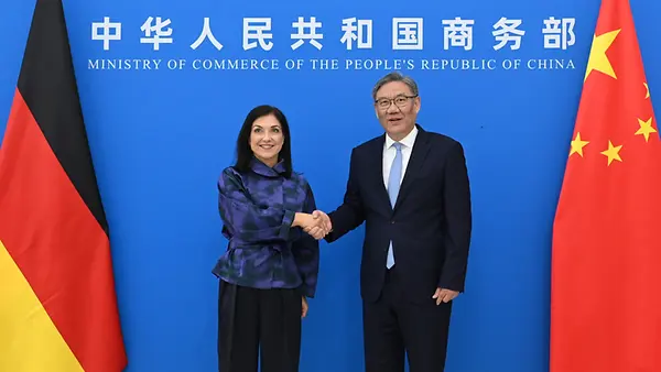 Vor blauer Wand mit Flaggen schütteln Bundeswirtschaftsministerin Katherina Reiche und der chinesische Handelsminister Wang Wentao die Hände. 