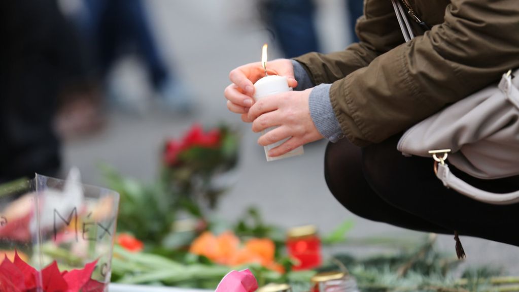Eine Frau mit einer Kerze am Gedenkplatz mit Blumen