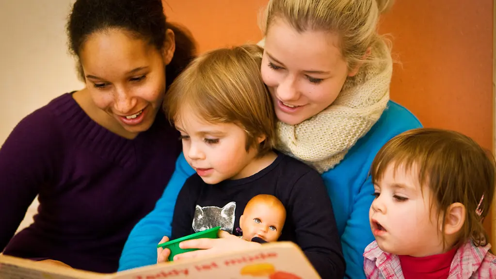 Kinderbetreuerin liest Kindern aus Buch vor.